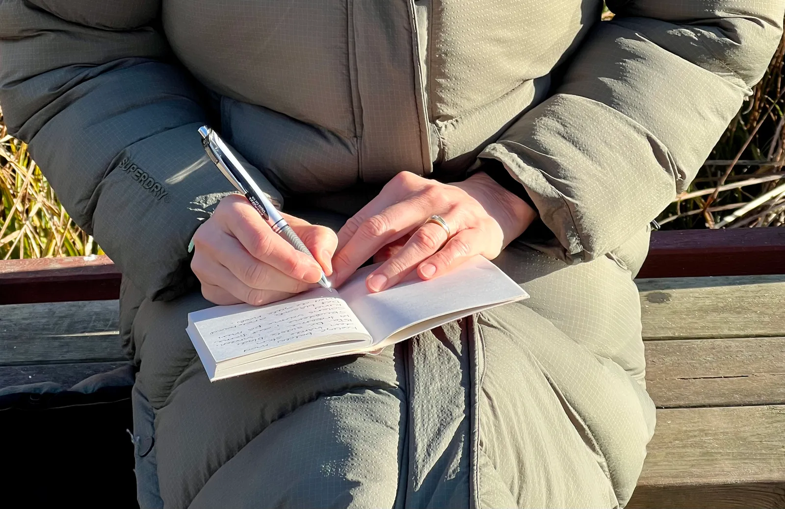 En person skriver i en notesbog udendørs i solen